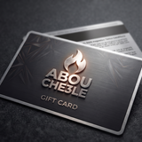 A metallic gift card with a brushed dark gray finish, featuring the brand name 'ABOU CHE3LE' in raised silver lettering beneath a stylized flame logo. The card is shown at an angle on a dark textured surface, with a second card partially visible behind it. -  Abou Che3le Gift Card -  Abouche3le