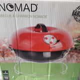 A red and black BE NOMAD charcoal barbecue grill in its original retail packaging, featuring a green base on the box with product imagery of food and herbs. -  Be Nomad Transportable Charcoal Barbecue Grill -  Abouche3le