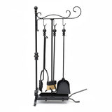Black wrought iron fireplace tool set with a poker, tongs, brush, and stand, photographed outdoors against a concrete pillar on patterned tile flooring.