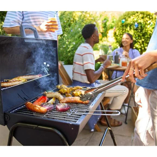 People grilling outdoors with a focus on the GRILLMEISTER Kansas Charcoal Barrel BBQ Grill