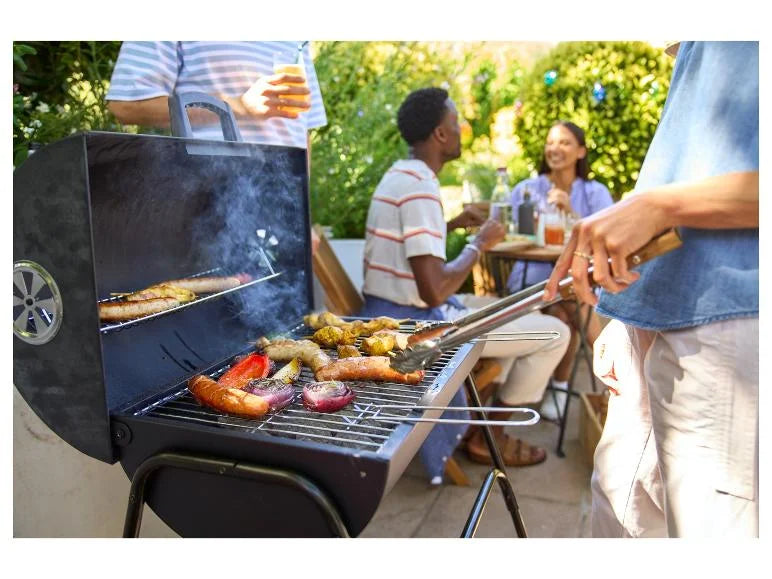 People grilling outdoors with a focus on the GRILLMEISTER Kansas Charcoal Barrel BBQ Grill