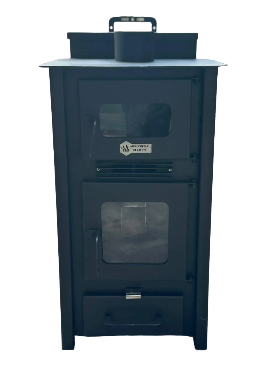 A black metal wood-burning stove or fireplace with two glass-front doors and a top handle, photographed outdoors on a paved surface with cars and a wall blurred in the background.