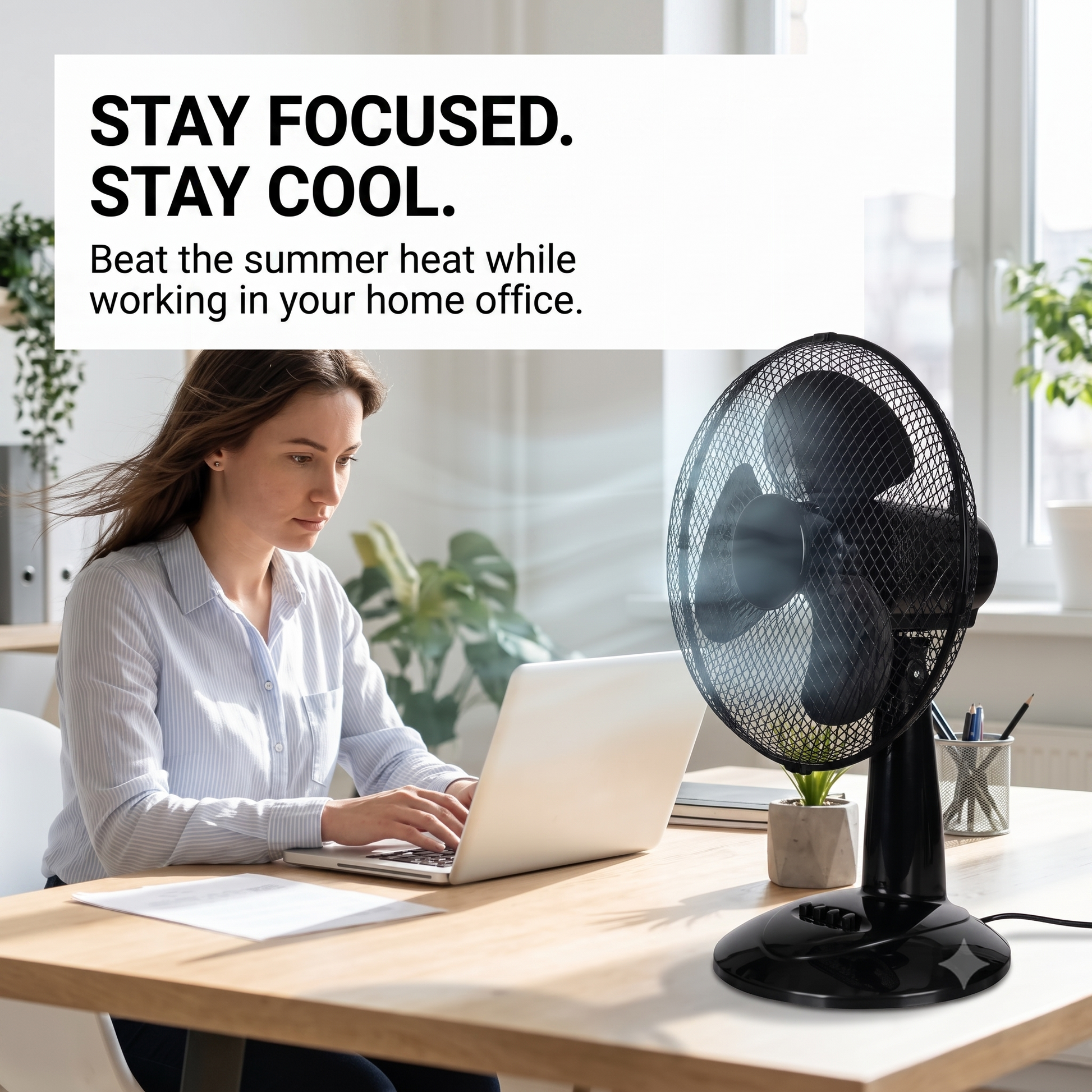 A woman working on a laptop at a wooden desk next to a black pedestal LEX XXL Table Fan Premium Wind Machine in a bright home office setting. A text overlay at the top reads 'STAY FOCUSED.